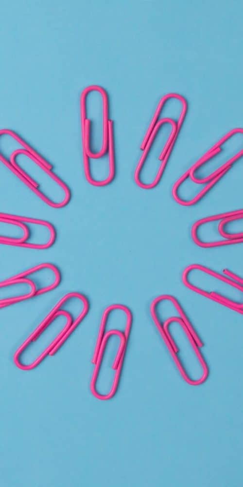 Pink Paperclips arranged in a circle on blue paper